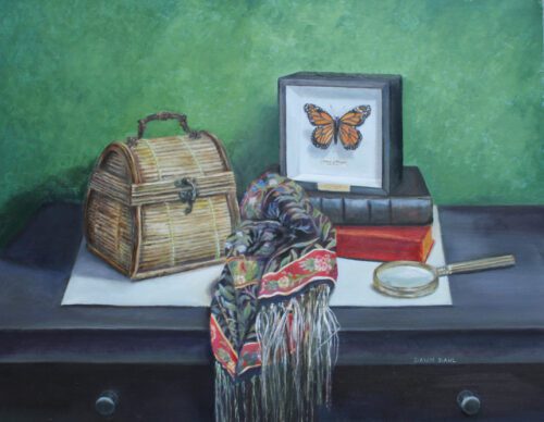a ratan purse, shawl, magnifying glass, two books, and a framed monarch butterfly all rest on a black table with a green wall behind it
