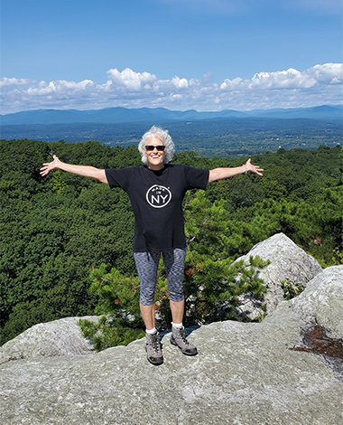 Jill Baratta standing on rock with mountains and sky in background